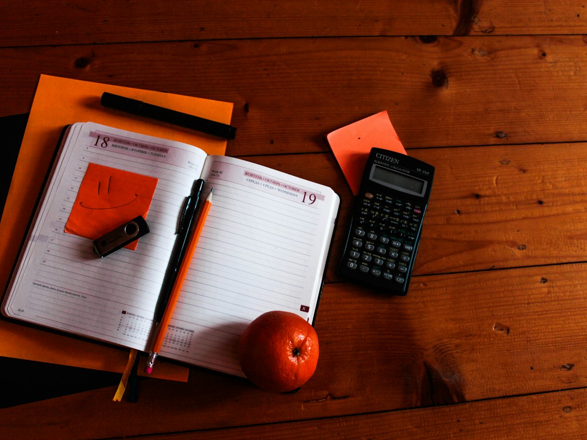 An open diary, pen and calculator on a wooden desk